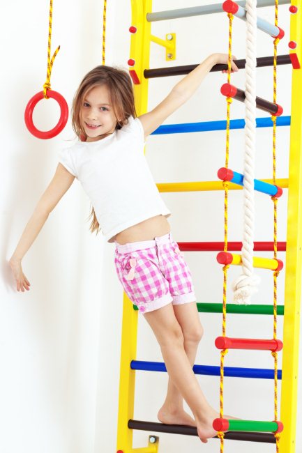 Спортивный уголок для ребенка - девочка играет на шведской стенке