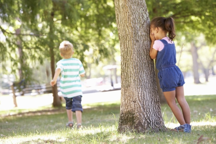 Играем в прятки с детьми - девочка у дерева считает с закрытыми глазами