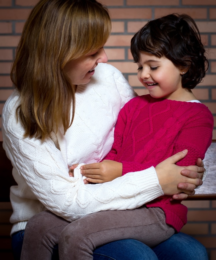Как отучить ребенка обзываться - девочка внимательно слушает маму, сидя у нее на коленях